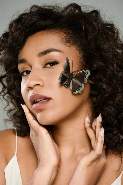 Mujer afroamericana bonita con mariposa en la cara aislada en gris — Stock Photo