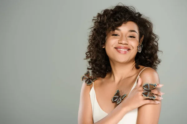Joyful african american woman with butterflies on body and cheek posing isolated on grey — Stock Photo