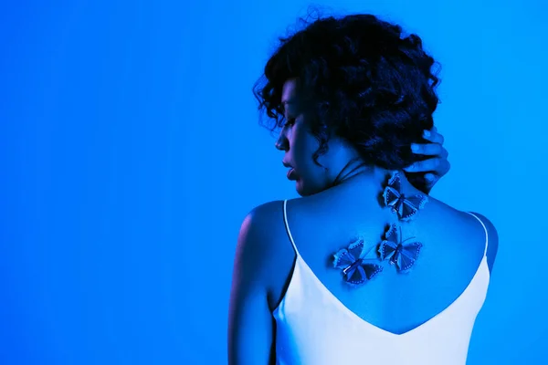 Jeune femme afro-américaine avec des papillons sur le dos posant isolé sur bleu vif — Photo de stock