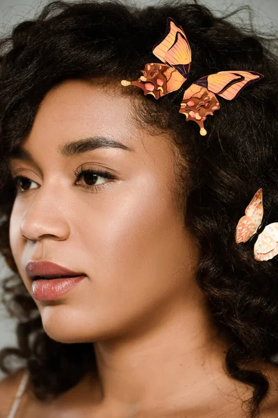 Nahaufnahme einer hübschen afrikanisch-amerikanischen Frau mit Schmetterlingen im Haar, die isoliert auf grau posiert — Stockfoto