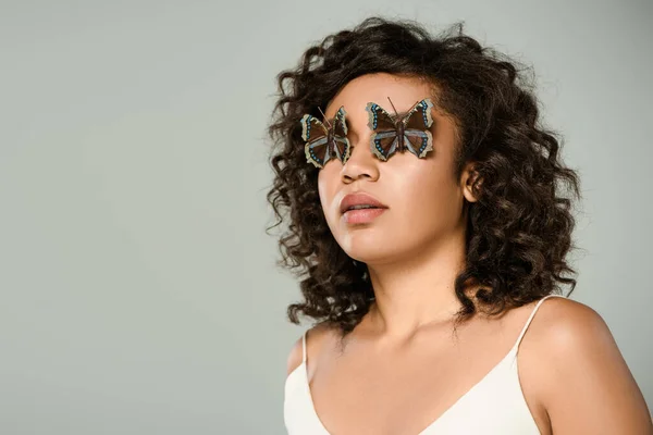 Femme afro-américaine bouclée avec des papillons sur les yeux isolés sur gris — Photo de stock