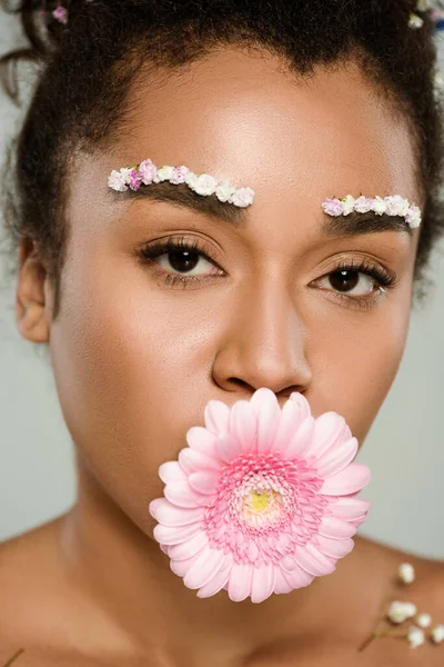 Крупным планом африканской американки с цветами на бровях и волосами с герберой во рту, изолированными на сером — стоковое фото