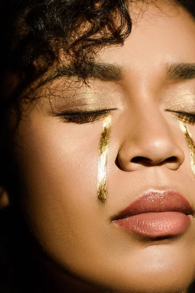 Primer plano de la mujer afroamericana con lágrimas de oro en las mejillas y ojos cerrados - foto de stock