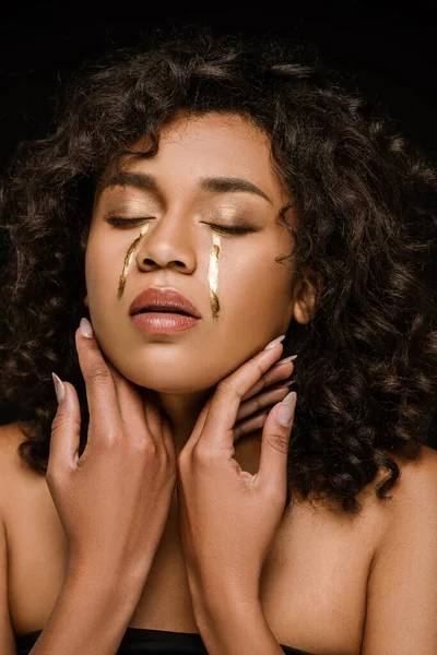 Mulher afro-americana com lágrimas douradas nas bochechas e olhos fechados isolados no preto — Fotografia de Stock