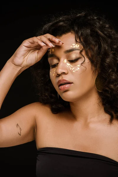 Mujer afroamericana tatuada con pintura dorada en mejillas aisladas en negro - foto de stock
