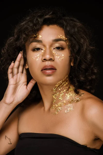 Curly african american woman with golden paint looking at camera isolated on black — Stock Photo