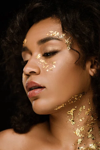Close up of young african american woman with golden paint on face and neck isolated on black — Stock Photo