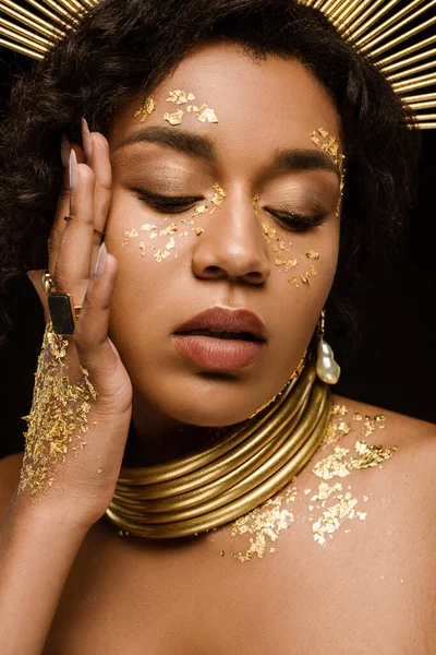 Joven modelo afroamericano con accesorios dorados y pintura en la cara aislada en negro - foto de stock