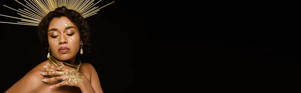 Кучерява афроамериканська жінка з золотими аксесуарами і фарбою на обличчі позує ізольовано на чорному, банер — стокове фото