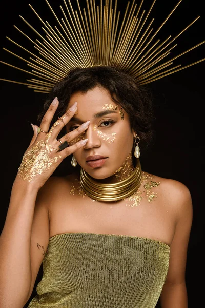 Bruna donna afroamericana con accessori dorati e vernice sul viso in posa isolata sul nero — Foto stock