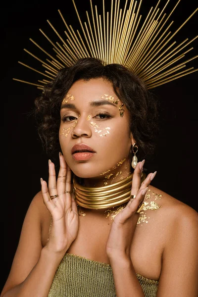Молодая африканская американка с золотым ожерельем и краской на лице, смотрящая на камеру, изолированную на черном — стоковое фото