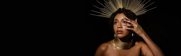 Tattooed african american woman with golden crown and paint on face looking up isolated on black, banner — Stock Photo