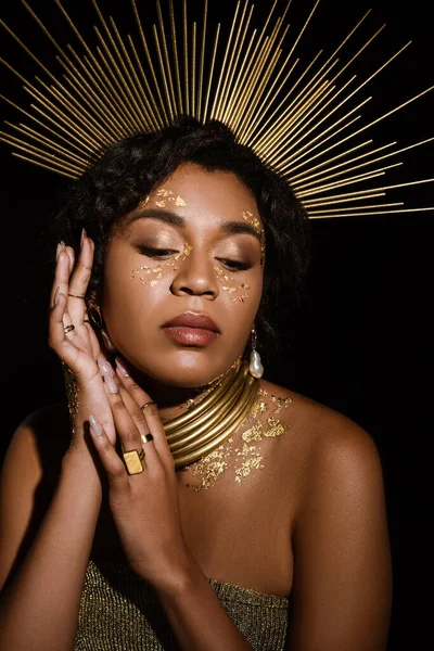Joven mujer afroamericana con collar de oro y pintura en las mejillas aisladas en negro - foto de stock