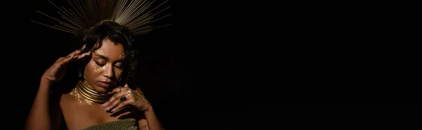 Молодая африканская американка с золотым ожерельем и короной позирует изолированно на черном, баннер — стоковое фото
