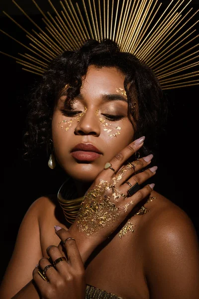 Morena mujer afroamericana con collar de oro y pintura en las mejillas aisladas en negro - foto de stock