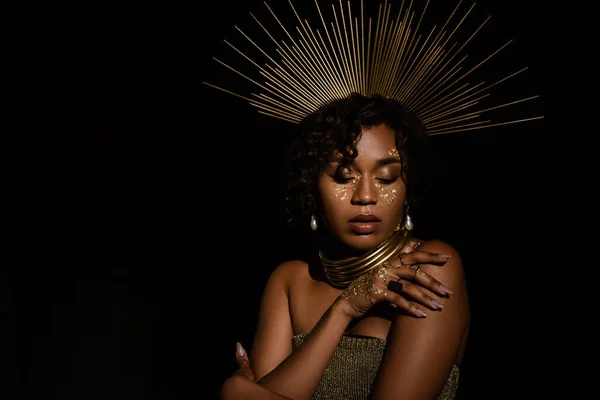 Confident african american woman with golden crown and paint on cheeks posing isolated on black — Stock Photo