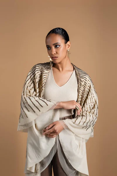 Brunette african american woman in golden jewelry covered in shawl posing isolated on beige — Stock Photo