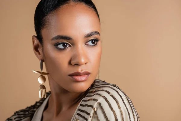 Ritratto di elegante donna afroamericana in orecchino dorato distolgendo lo sguardo isolato sul beige — Foto stock