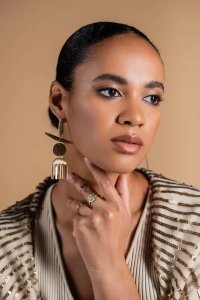Elegant african american woman in golden jewelry touching neck isolated on beige — Stock Photo