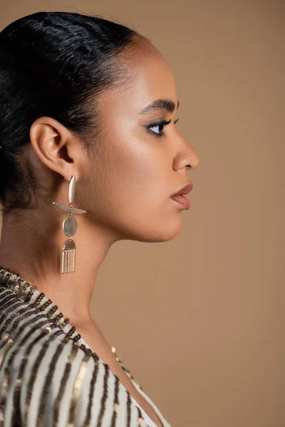 Side view of young african american woman in luxurious golden jewelry isolated on beige — Stock Photo