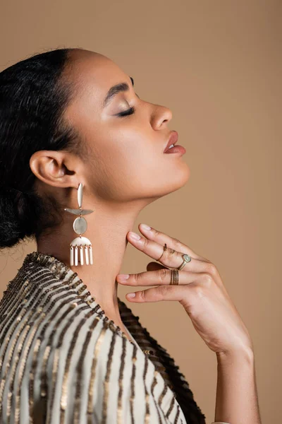 Side view of young african american woman in luxurious golden jewelry posing isolated on beige — Stock Photo
