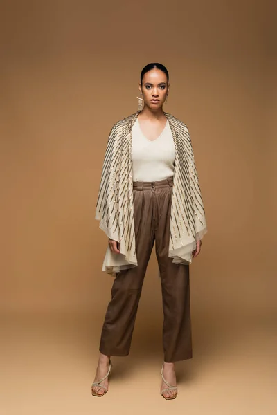 Full length of stylish african american woman in golden shawl standing on beige — Stock Photo