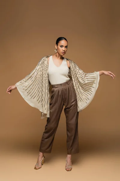 Full length of stylish african american woman in golden shawl gesturing on beige — Stock Photo