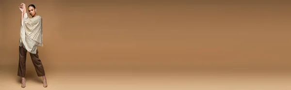Pleine longueur de femme brune afro-américaine en bijoux dorés et châle posant sur beige, bannière — Photo de stock