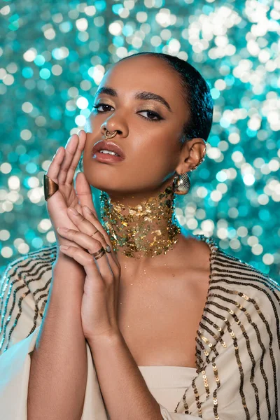Brunette afro-américaine avec châle brillant et or sur le cou posant sur fond bleu étincelant — Photo de stock