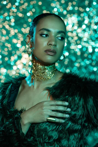 Mujer afroamericana con estilo en chaqueta de piel sintética y oro en el cuello posando sobre fondo azul brillante - foto de stock