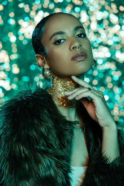 Portrait of fashionable african american woman in faux fur jacket with golden foil on neck posing on sparkling background — Stock Photo