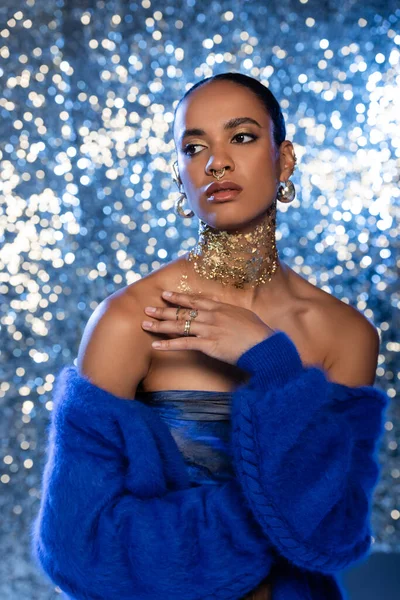Elegante afrikanisch-amerikanische Frau in blauem Pullover und Folie am Hals auf glitzerndem Hintergrund — Stockfoto