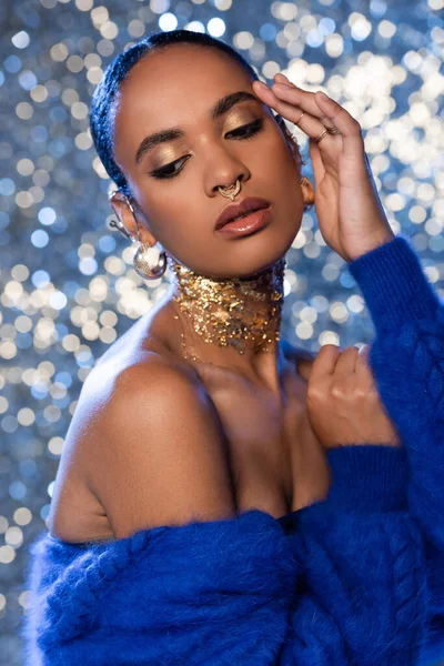 Modelo afroamericano de moda con accesorios dorados y chaqueta de piel sintética azul sobre fondo brillante - foto de stock