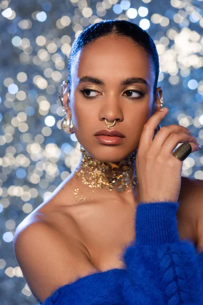 Retrato del modelo afroamericano de moda con accesorios dorados mirando hacia otro lado sobre un fondo brillante - foto de stock