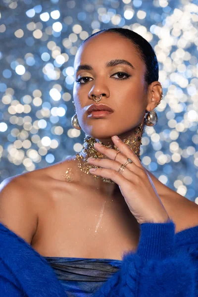 Portrait of trendy african american woman with makeup and golden foil on neck posing on sparkling background — Stock Photo