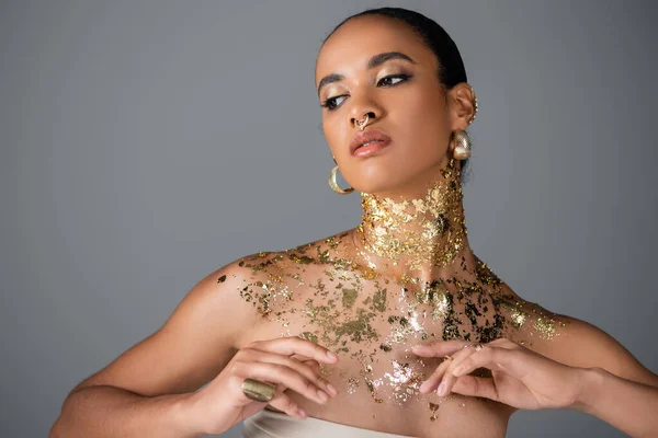Трендовая африканская модель с золотой фольгой на груди позирует на сером фоне — стоковое фото