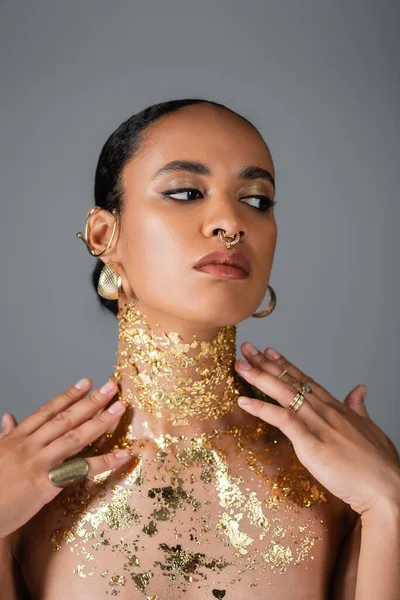 Елегантна афроамериканська модель із золотою фольгою на грудях, що торкається шиї, ізольована на сірому — стокове фото