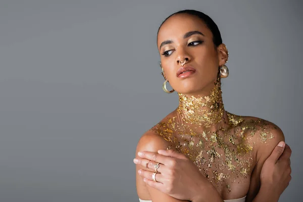 Jolie modèle afro-américain avec feuille d'or sur la poitrine touchant les épaules isolées sur gris — Photo de stock