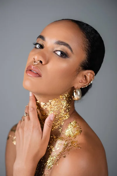 Portrait of trendy african american model touching golden foil on neck isolated on grey — Stock Photo