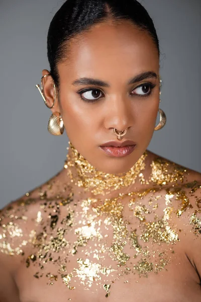 Retrato de modelo afroamericano de moda con accesorios y lámina dorada posando aislada sobre gris - foto de stock