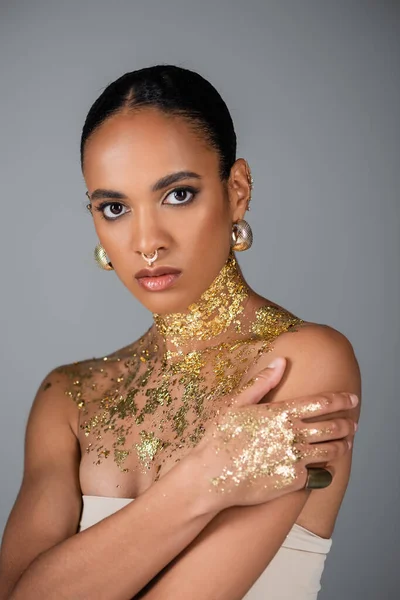 Fashionable african american model with golden foil on chest and piercing looking at camera isolated on grey — Stock Photo