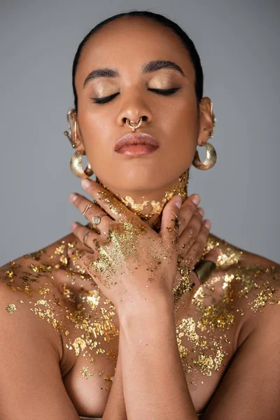 Fashionable african american woman touching neck with golden foil isolated on grey — Stock Photo