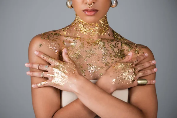 Vue partielle du modèle afro-américain avec feuille d'or sur les mains et la poitrine posant isolé sur gris — Photo de stock