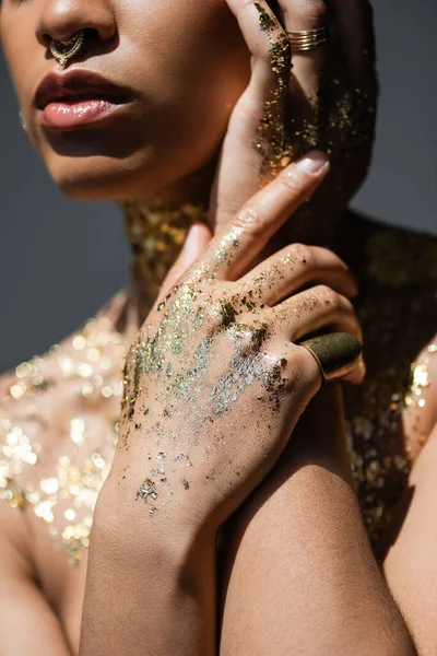 Vue recadrée du modèle afro-américain tendance avec feuille d'or sur les mains et le corps isolé sur gris avec de la lumière — Photo de stock