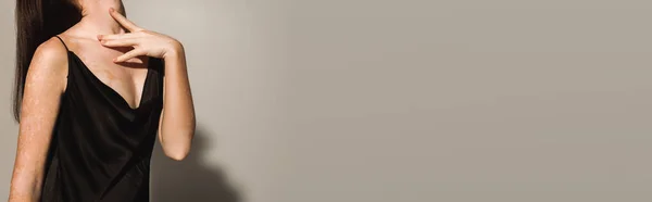 Обрізаний вид брюнетки в чорному платті, торкаючись шиї на сірому фоні, банер — стокове фото