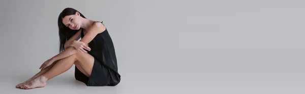 Modelo joven con vitiligo en vestido de satén sentado sobre fondo gris con espacio para copiar, pancarta - foto de stock