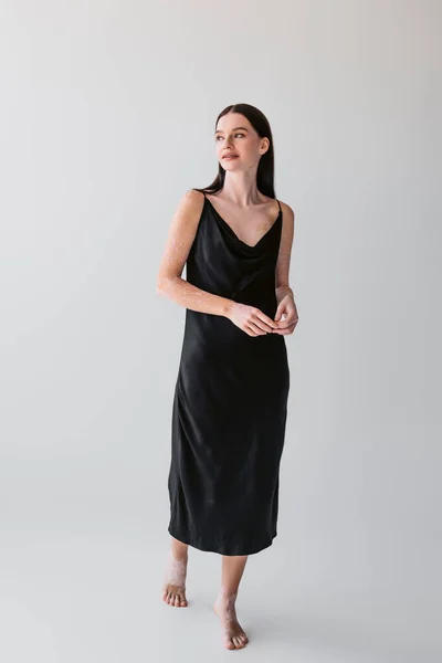 Full length of stylish model with vitiligo posing in silk dress on grey background — Stock Photo