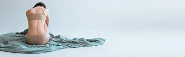 Вид брюнетки с хроническим заболеванием кожи витилиго сидя на одеяле на сером фоне, баннер — стоковое фото