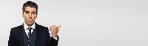 Empresário surpreso em terno apontando com polegar de distância isolado em cinza, banner — Fotografia de Stock