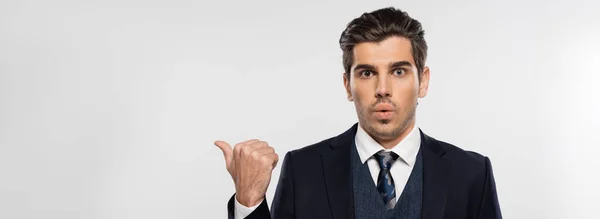 Приголомшений бізнесмен у костюмі, вказуючи на великий палець ізольовано на сірому, банер — стокове фото